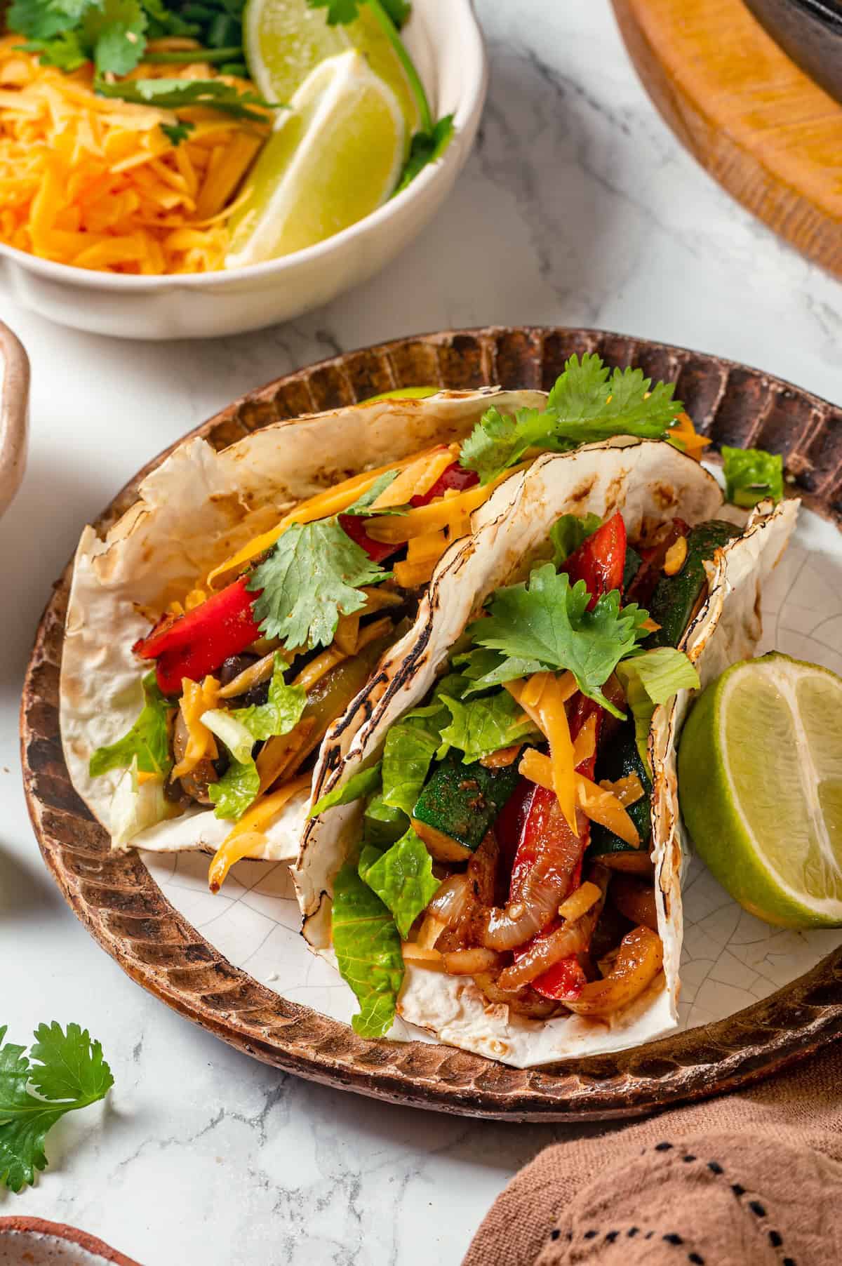 Two vegetarian fajitas on a plate with cheese and cilantro on top.