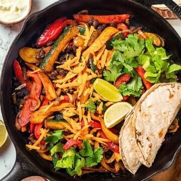 Close up of a vegetarian fajitas skillet with peppers, zucchini and black beans in a cast iron pan with charred tortillas to the side.