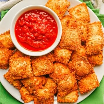 Close up of a round white plate filled with Air Fryer fried ravioli and a small white bowl with marinara for a dipping sauce.