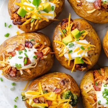 Close up of a platter of a baked potato bar with different fillings in each potato and toppings on top.