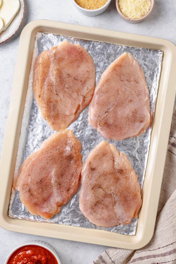 Flattened chicken breasts on a foil lined baking sheet.