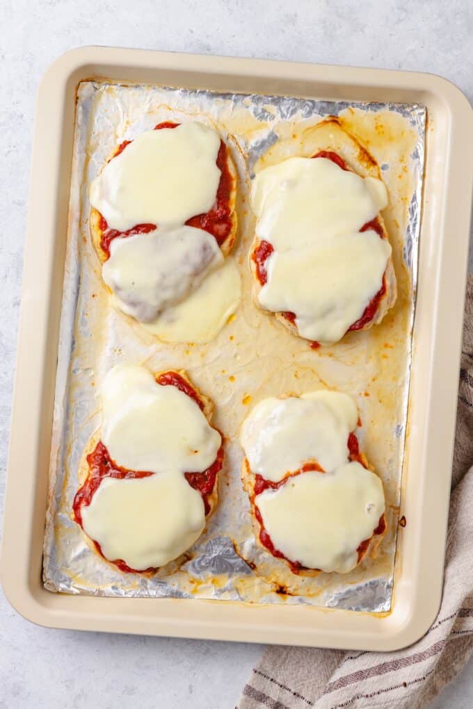 Melted mozzarella cheese and marinara on top of chicken breasts on a foil lined sheet pan.