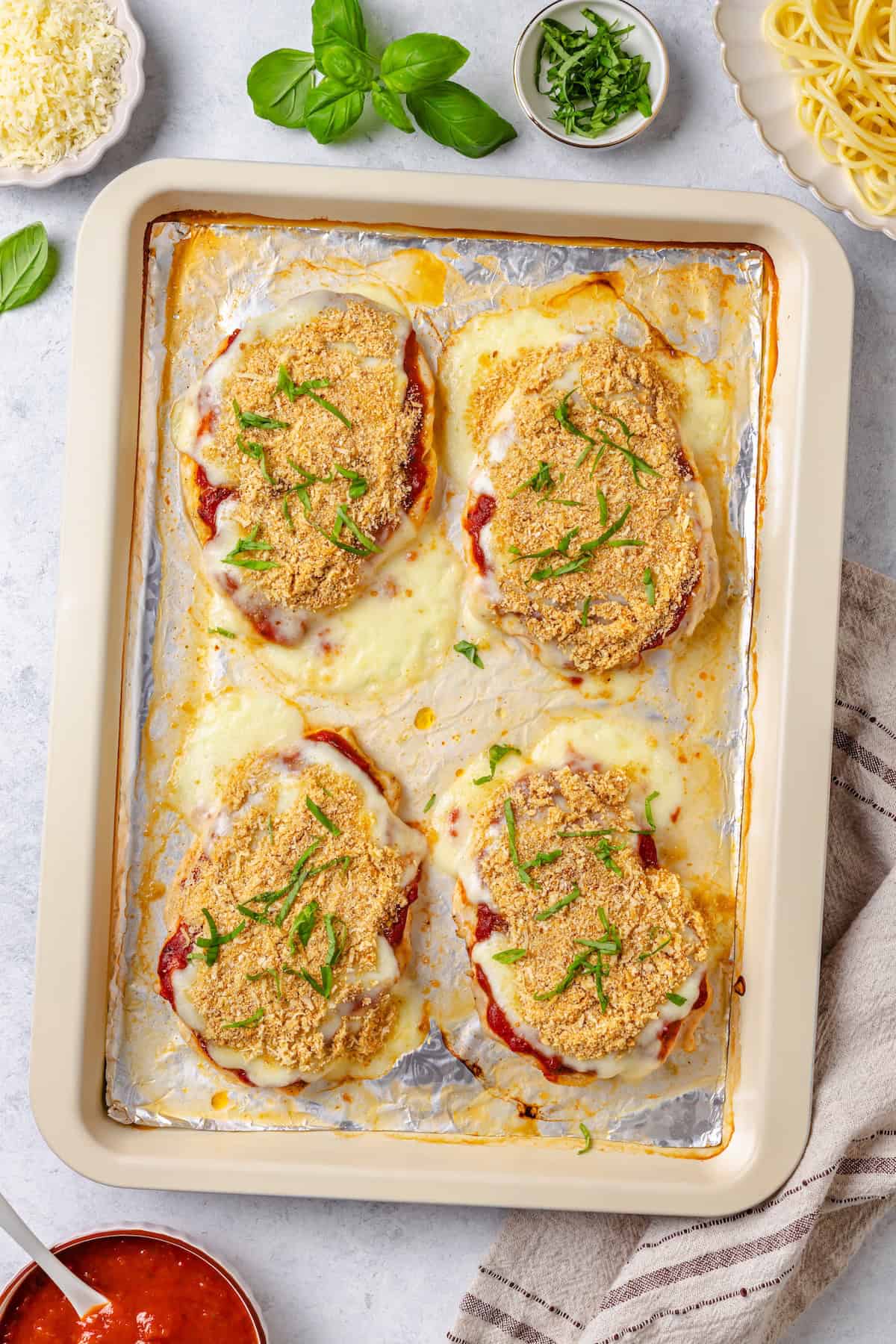 Sheet pan chicken Parm on a foil lined baking sheet with fresh basil sprinkled on top.