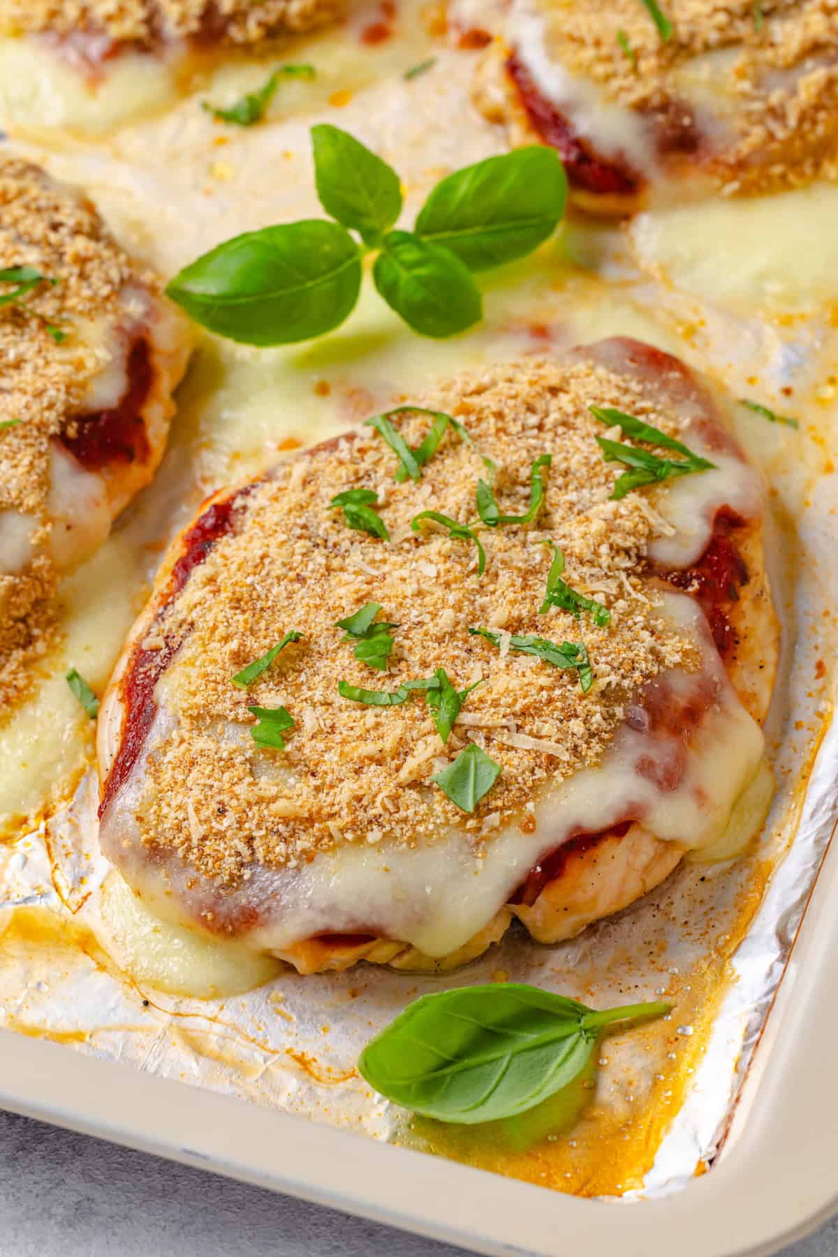 Close up of sheet pan chicken Parm on a foil lined baking sheet with fresh basil sprinkled on top.