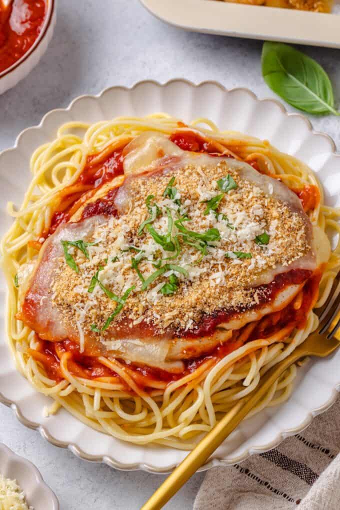 Chicken Parm served on top of hot cooked spaghetti and marinara sauce on a plate with a fork to the side.