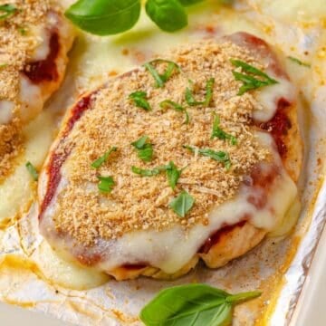 Close up of a chicken breast roasted chicken Parm on a foil lined baking sheet.