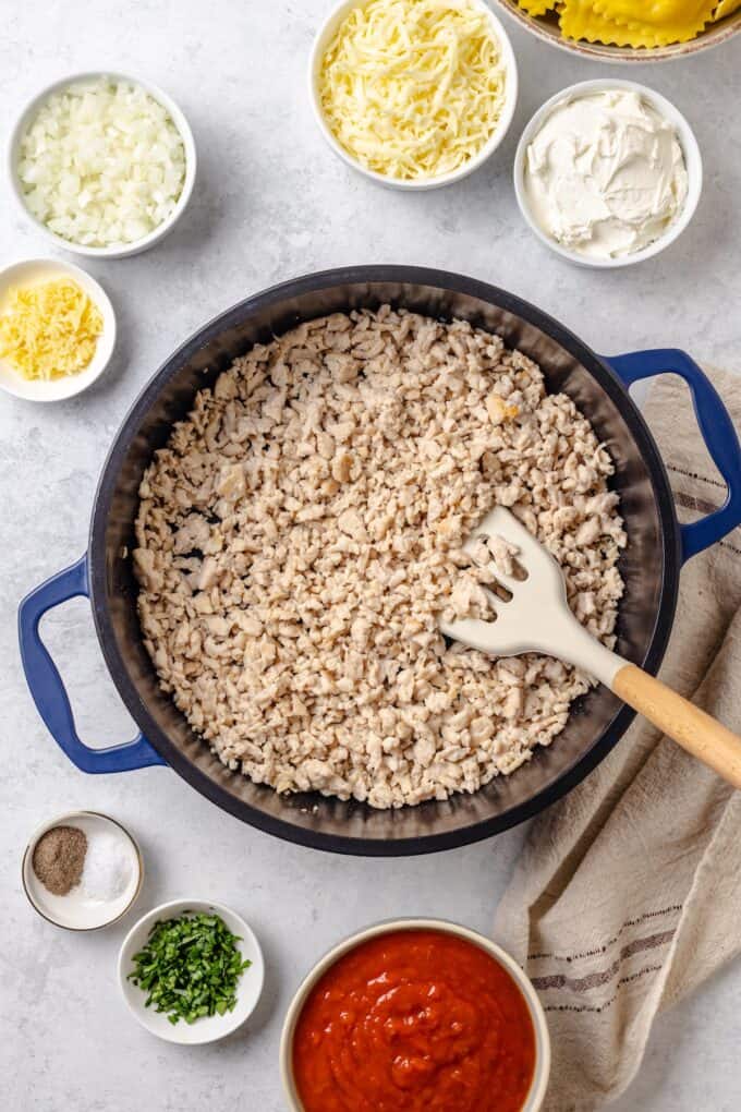 Cooked ground turkey in a large pot with bowls of other ingredients surrounding it to be added in.