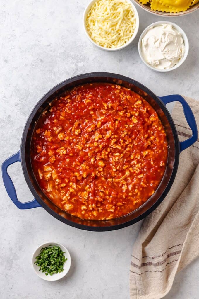 A saucy ground turkey mixture in a pot with bowls of cheese and herbs to the side to be added in.