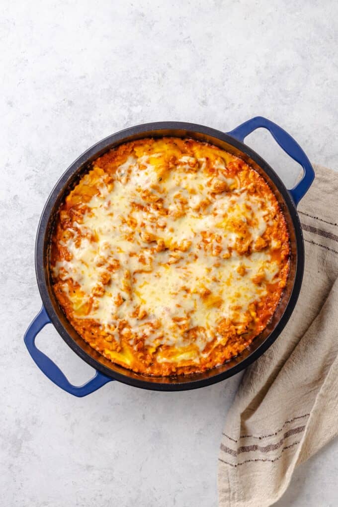 Melted mozzarella cheese on top of a large blue pot filled with a ground turkey ravioli lasagna mixture.