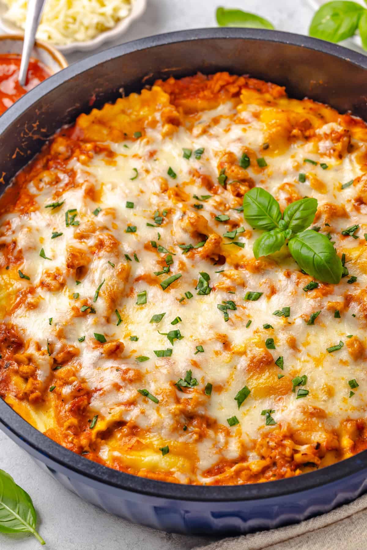 Skillet ravioli lasagna with ground turkey and topped with melted mozzarella and fresh basil in a large blue skillet.