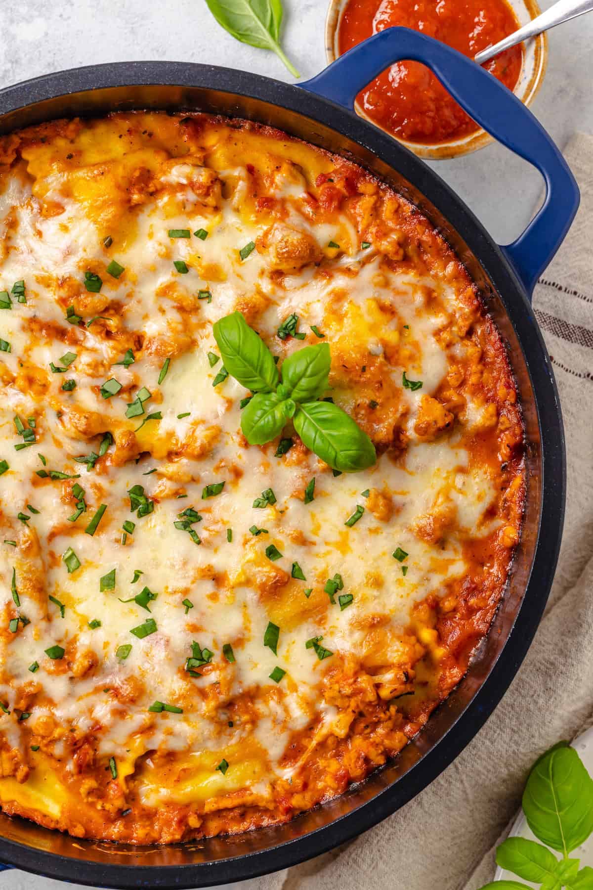 Close up of a skillet ravioli lasagna in a deep blue skillet with fresh basil on top.