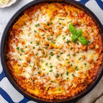 Close up of a ravioli lasagna in a deep blue skillet with melted mozzarella and fresh basil on top.