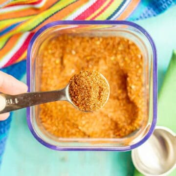 Close up of a hand lifting up a teaspoon full of a homemade southwest seasoning from a square storage container.