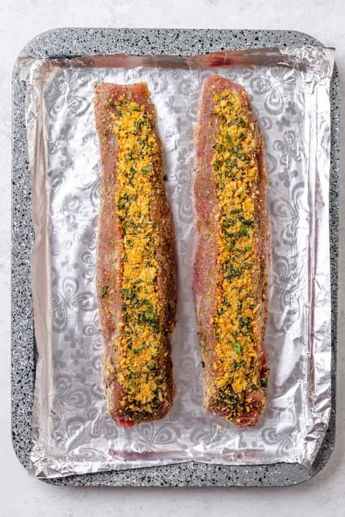 Two stuffed pork tenderloins on a foil lined baking sheet before being baked.