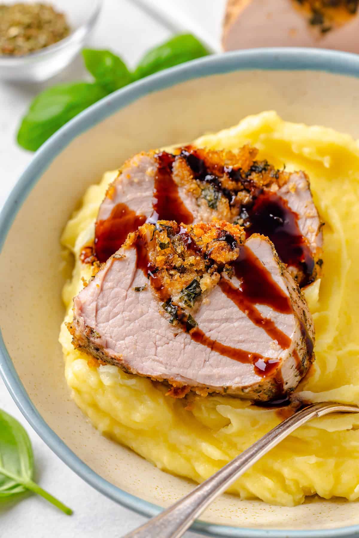 Two slices of a stuffed pork tenderloin served on top of creamy mashed potatoes in a low bowl.