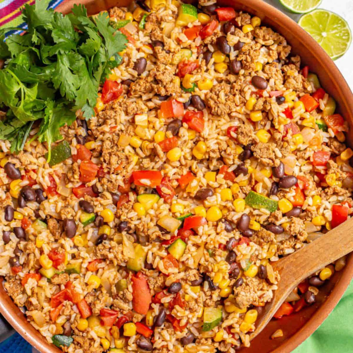 Close up of a copper skillet filled with a ground turkey and rice taco mixture with peppers, corn, zucchini and black beans.