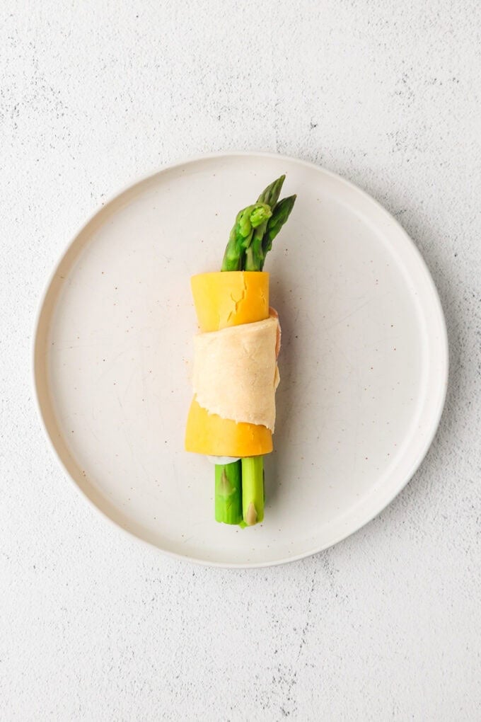 A triangle of crescent roll dough wrapped around asparagus pears, prosciutto and cheese.
