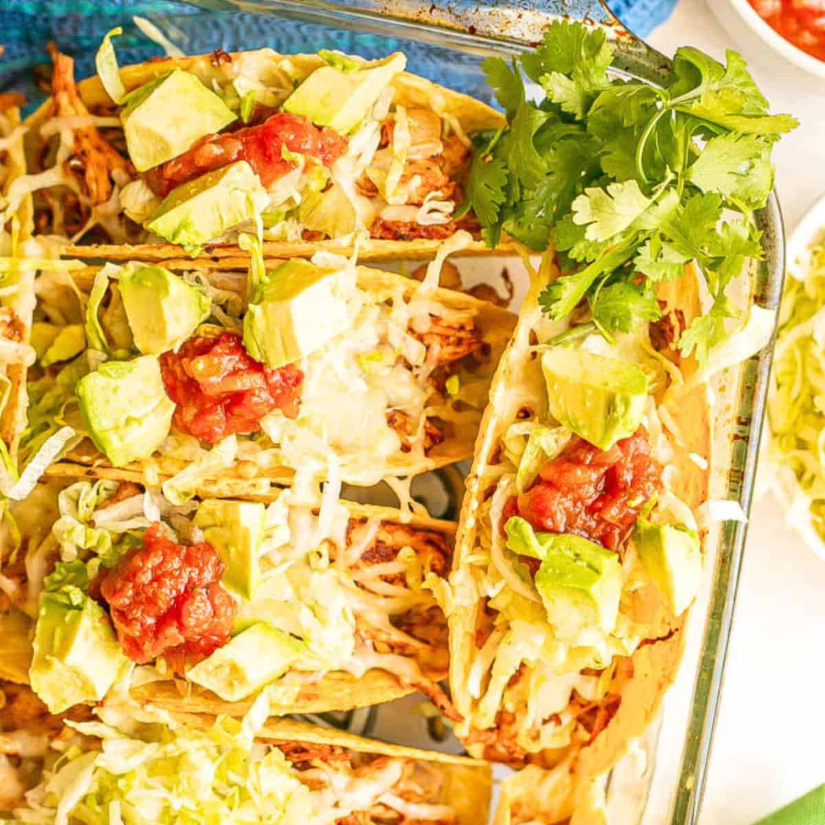 Close up of taco shells in a casserole dish filled with rice, shredded chicken and loaded with cheese, avocado and salsa for toppings.