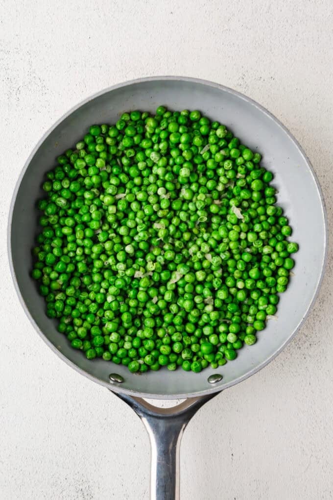 A skillet full of green peas with shallots.