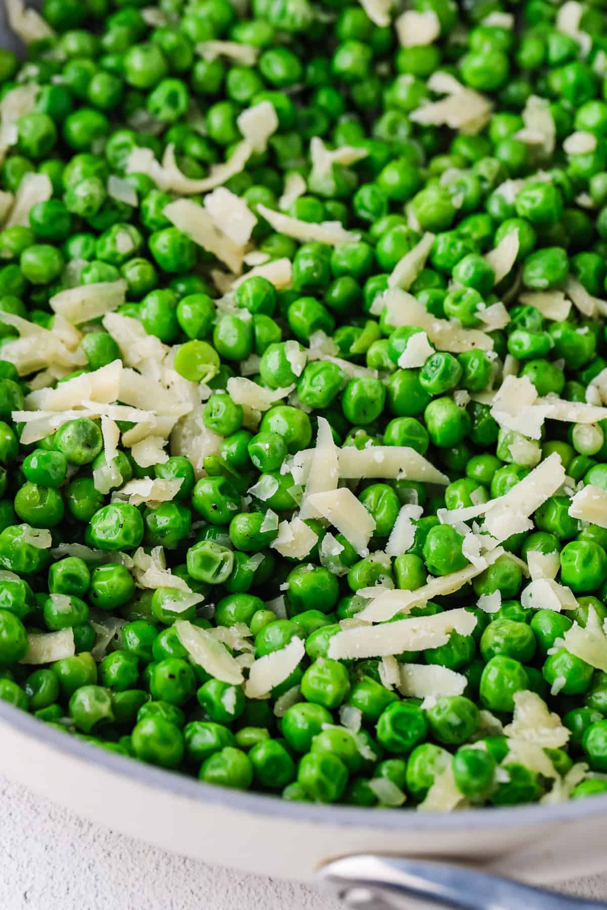 Close up of a skillet full of green peas with Parmesan cheese on top.