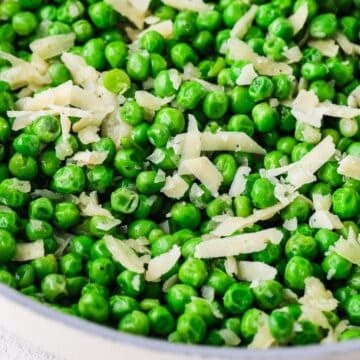 Close up of a skillet of warm green peas with Parmesan cheese on top.