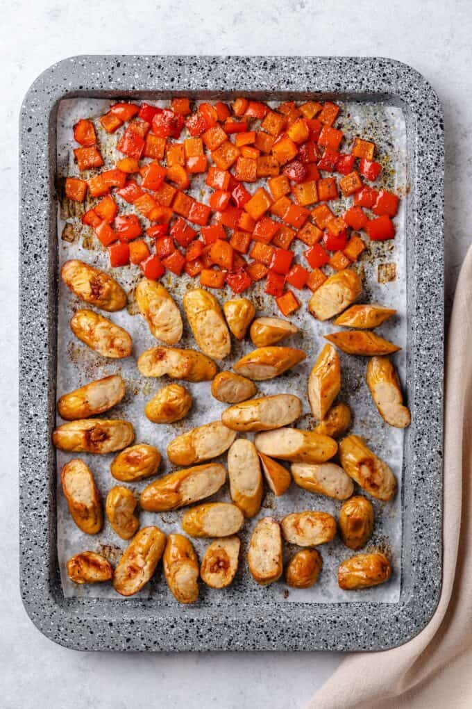 A sheet pan with diced red bell pepper and sliced chicken sausages after being roasted.