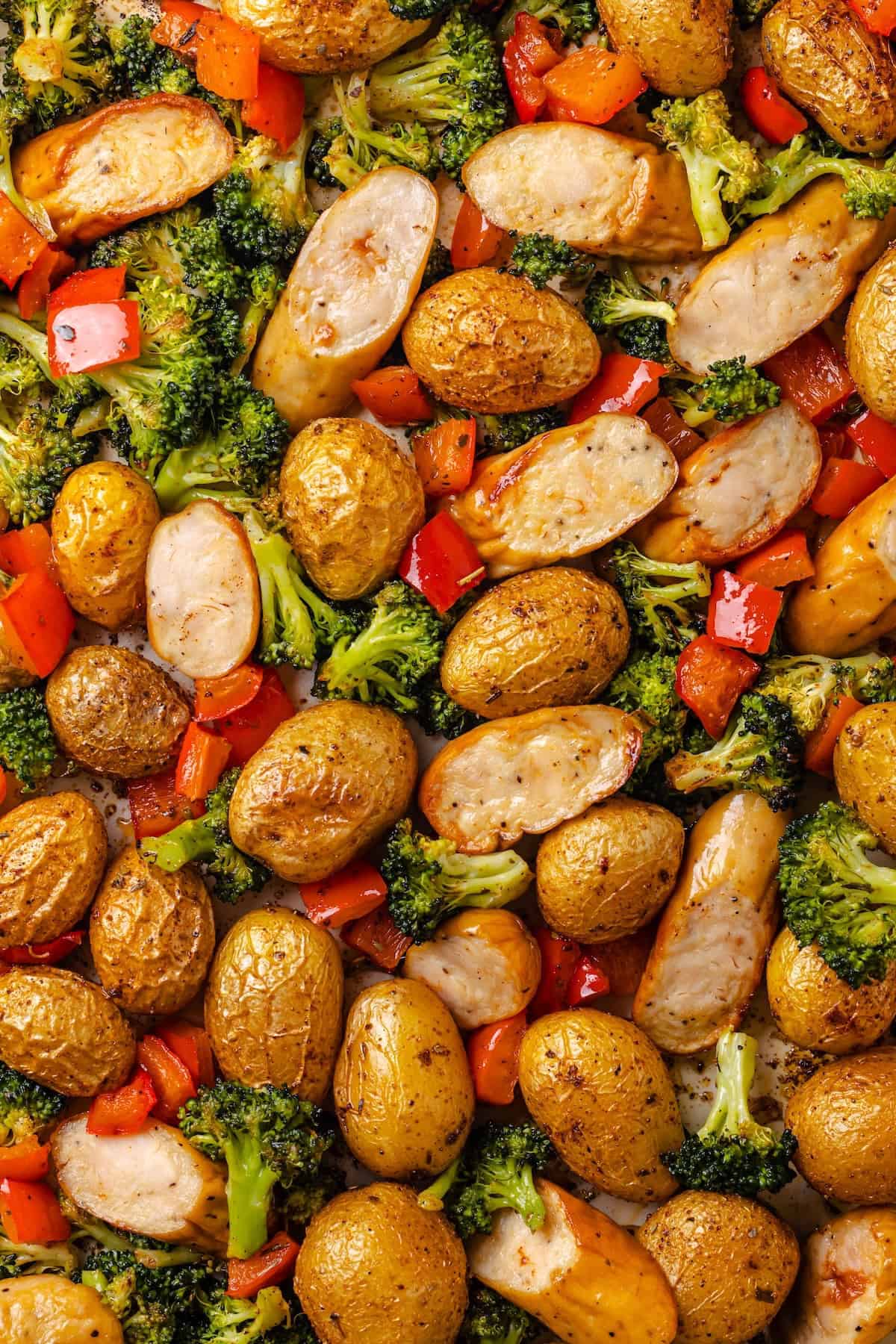 Close up of a sheet pan filled with chicken sausages, baby potatoes, red pepper and broccoli.