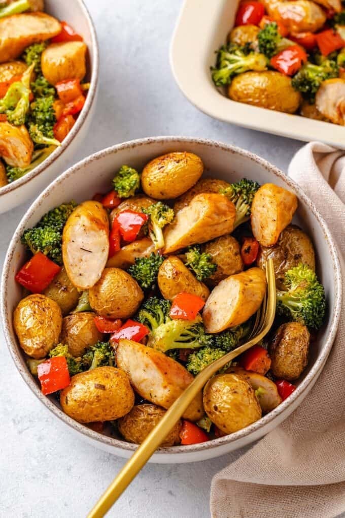 A bowl filled with chicken sausage, potatoes and broccoli with a fork resting on the side.