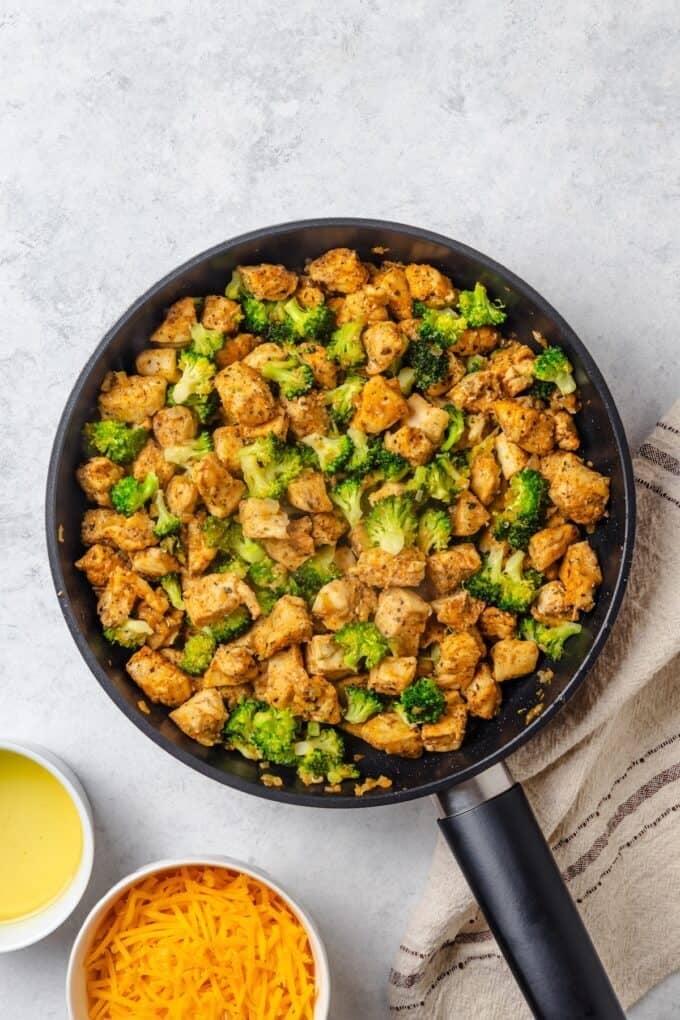 Cubed chicken and small broccoli florets being cooked together in a large skillet.
