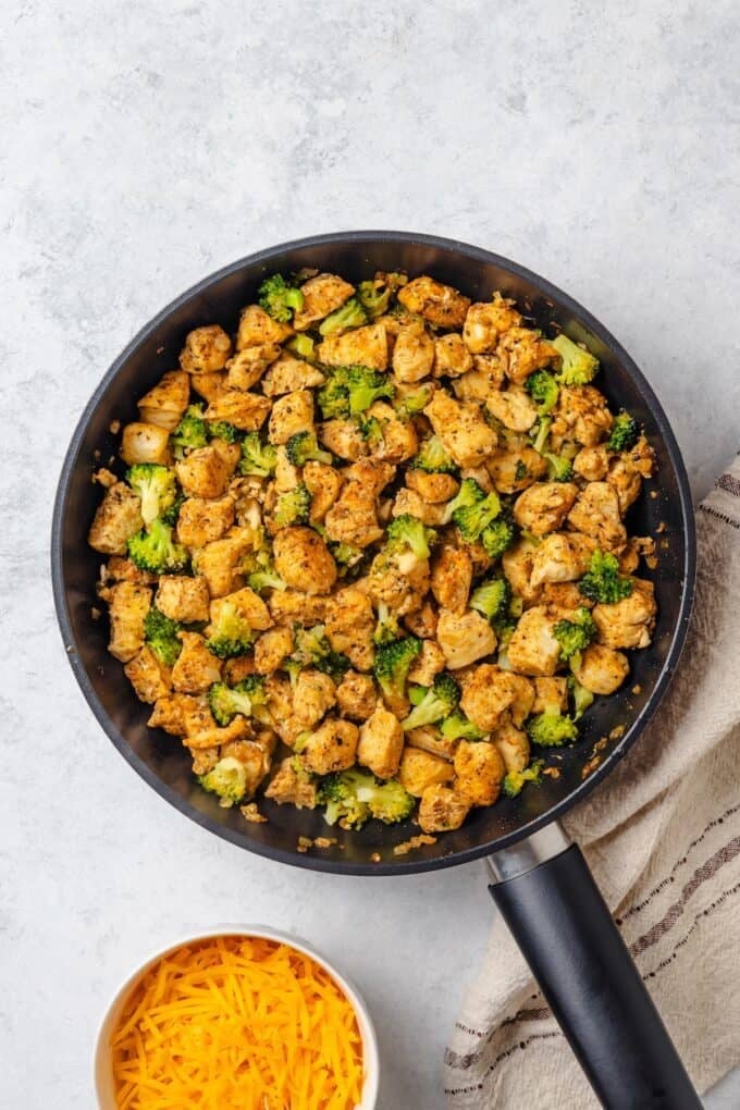 Cubed chicken and small broccoli florets after cooking together in a large skillet.