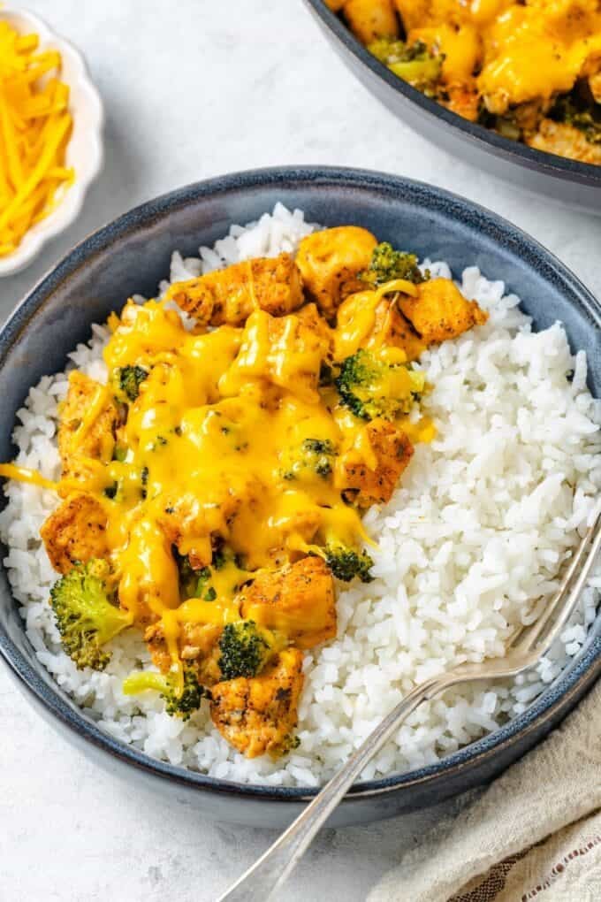 A bowl of steamed white rice with a cheesy cubed chicken and broccoli mixture on top and a fork to the side.
