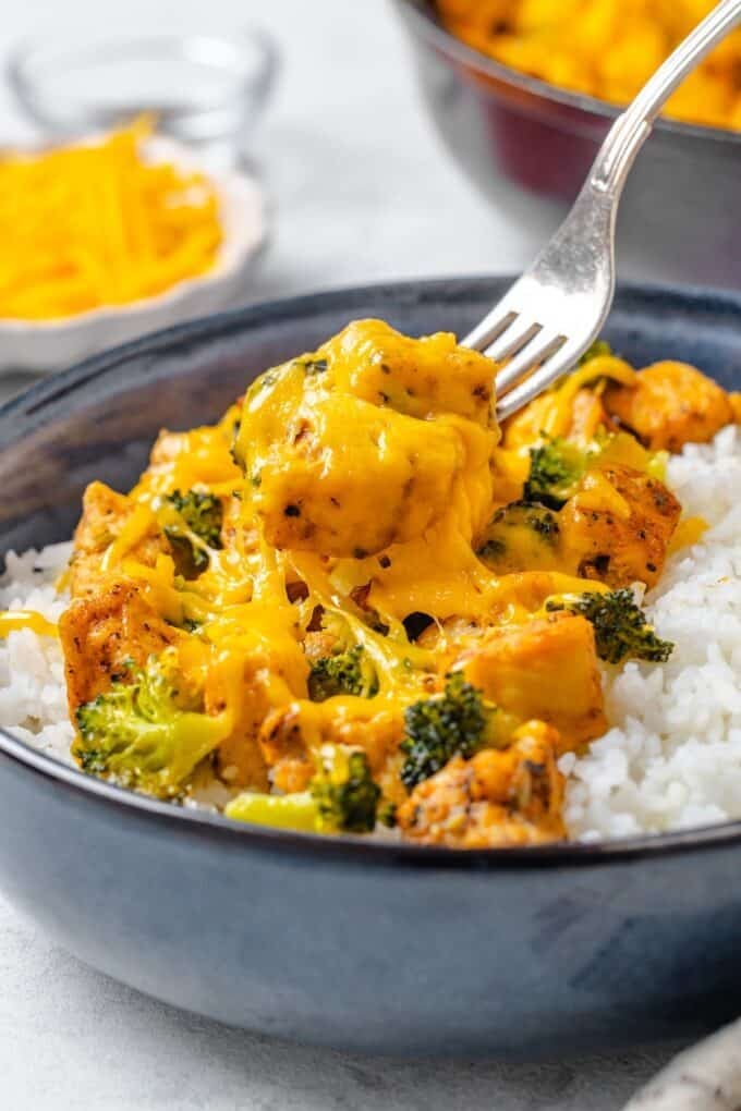 A fork lifting up a bite of cheesy chicken from a bowl.