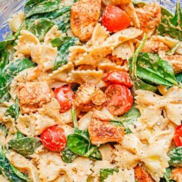 Close up of a bowl filled with a chicken pasta with spinach, tomatoes and a creamy hummus dressing.