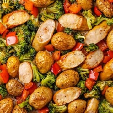 Close up of a sheet pan filled with chicken sausages, baby potatoes, red bell pepper and broccoli florets.