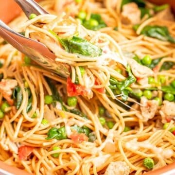 Tongs picking up a scoop of a one pot pasta with chicken sausage, spinach and peas from a large pot.