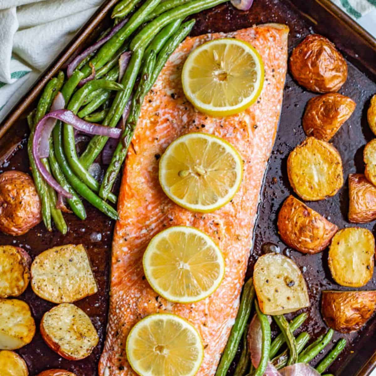 A sheet pan with roasted salmon topped with lemon slices, potatoes and green beans.
