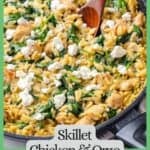 A wooden spoon resting in a dark skillet full of a creamy chicken, orzo and spinach mixture with feta cheese on top and a green text box around the image.