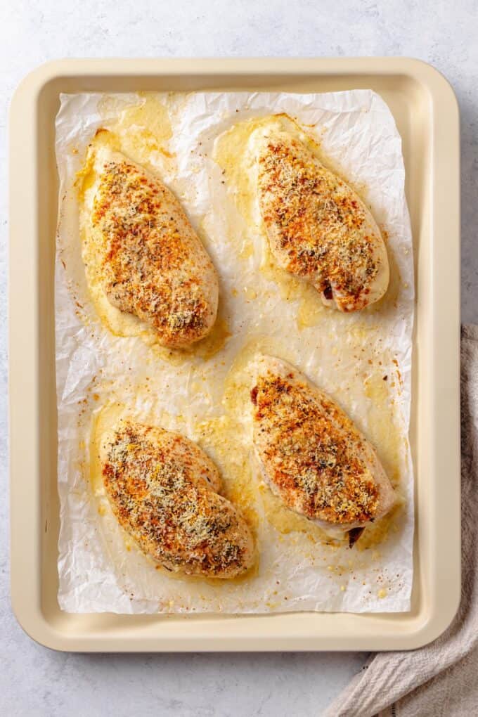 Baked chicken breasts on a parchment paper lined baking sheet.