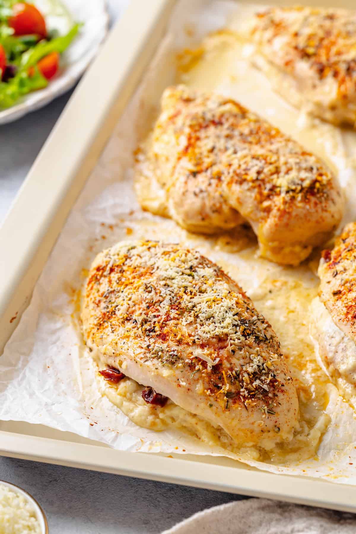 Baked cream cheese stuffed chicken breasts on a parchment paper lined baking sheet.