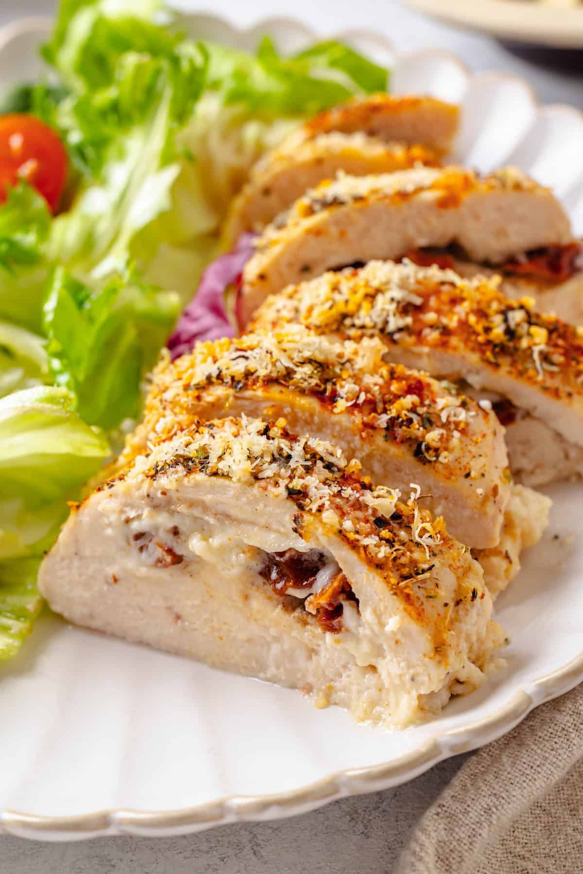 Sliced cream cheese stuffed chicken breast on a plate alongside a salad.