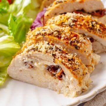 Close up of sliced cream cheese stuffed chicken breast on a plate alongside a salad.
