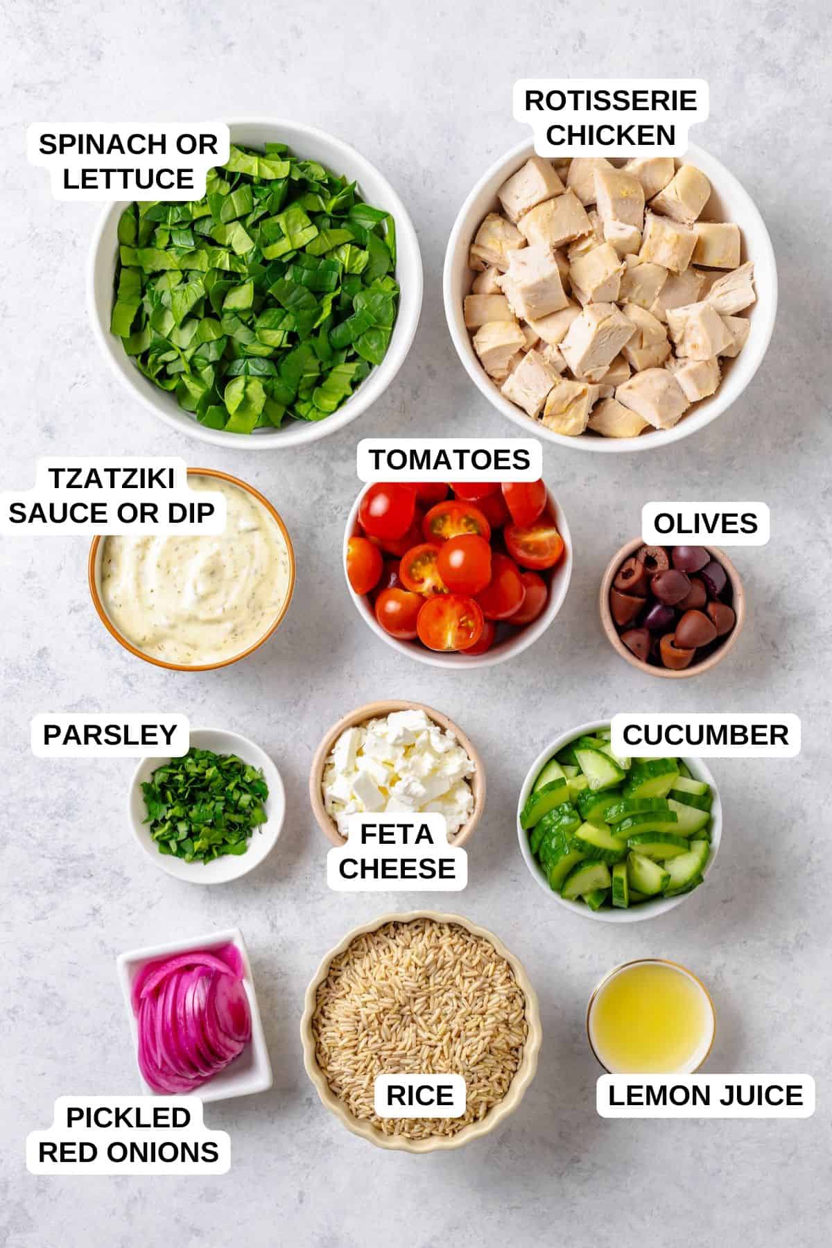 Ingredients laid out in separate bowls for making a Greek style chicken and rice and spinach bowl with veggies and tzatziki.