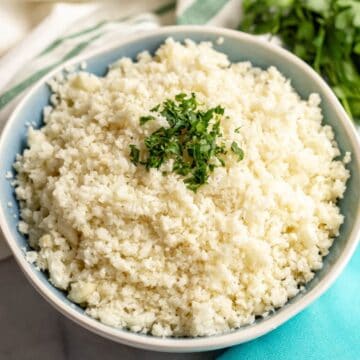 Close up of a bowl of homemade cauliflower rice with chopped fresh parsley sprinkled on the top.
