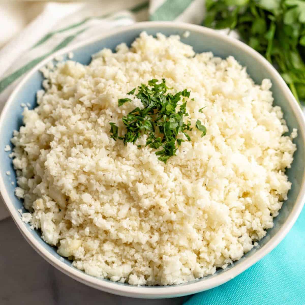 Close up of a bowl of homemade cauliflower rice with chopped fresh parsley sprinkled on the top.
