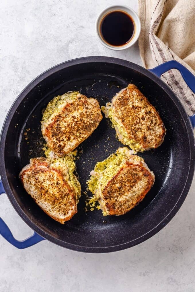 Four stuffed pork chops being seared in a skillet.