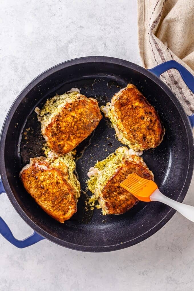 Four stuffed pork chops being seared in a skillet and brushed with balsamic vinegar.
