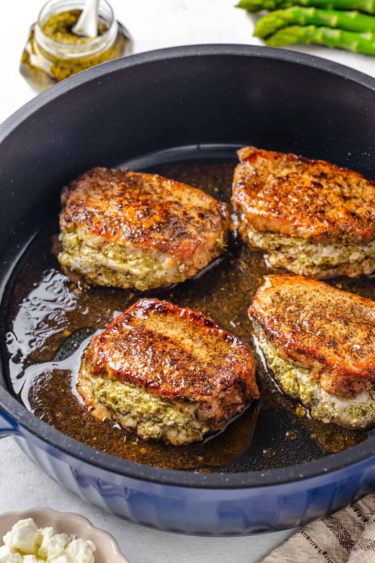 Four baked pesto stuffed pork chops in a blue skillet after being finished in the oven.