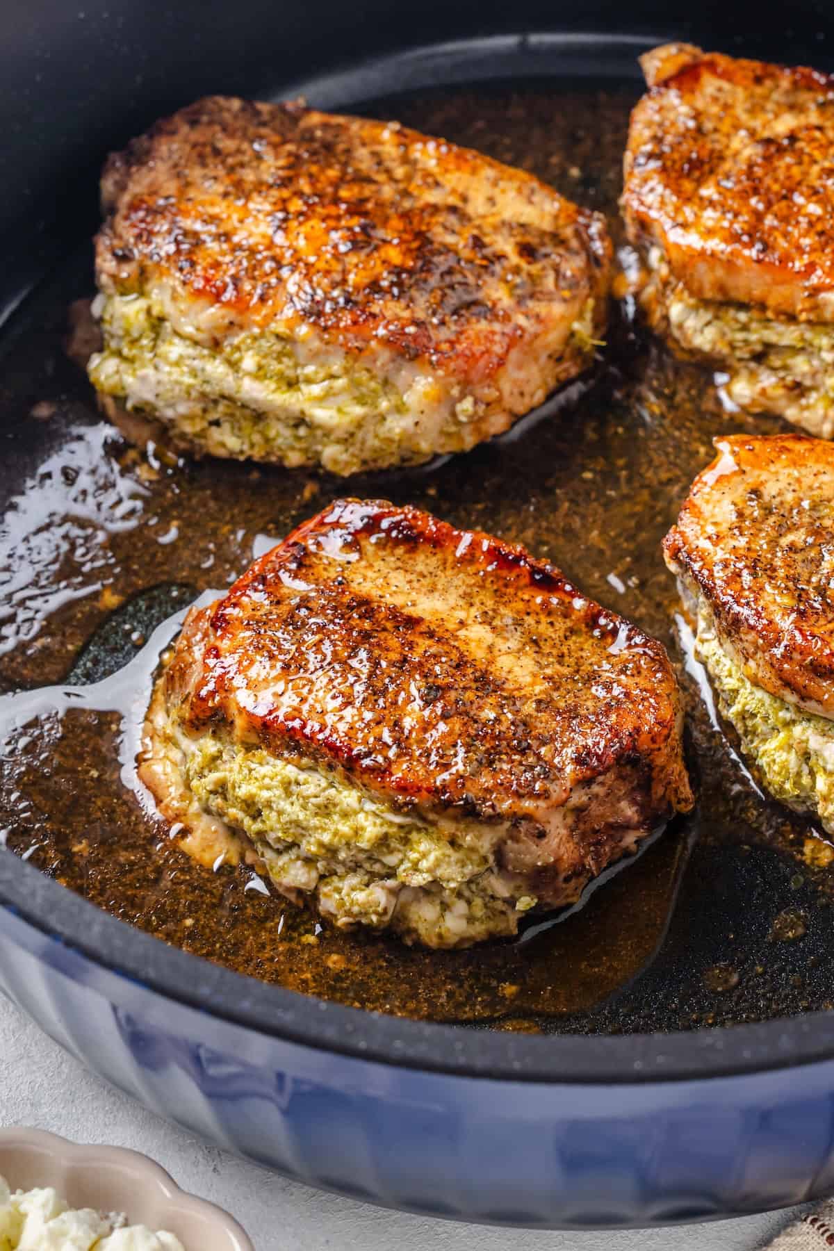 Close up of a balsamic vinegar brushed pork chop stuffed with pesto and feta cheese in a blue skillet.