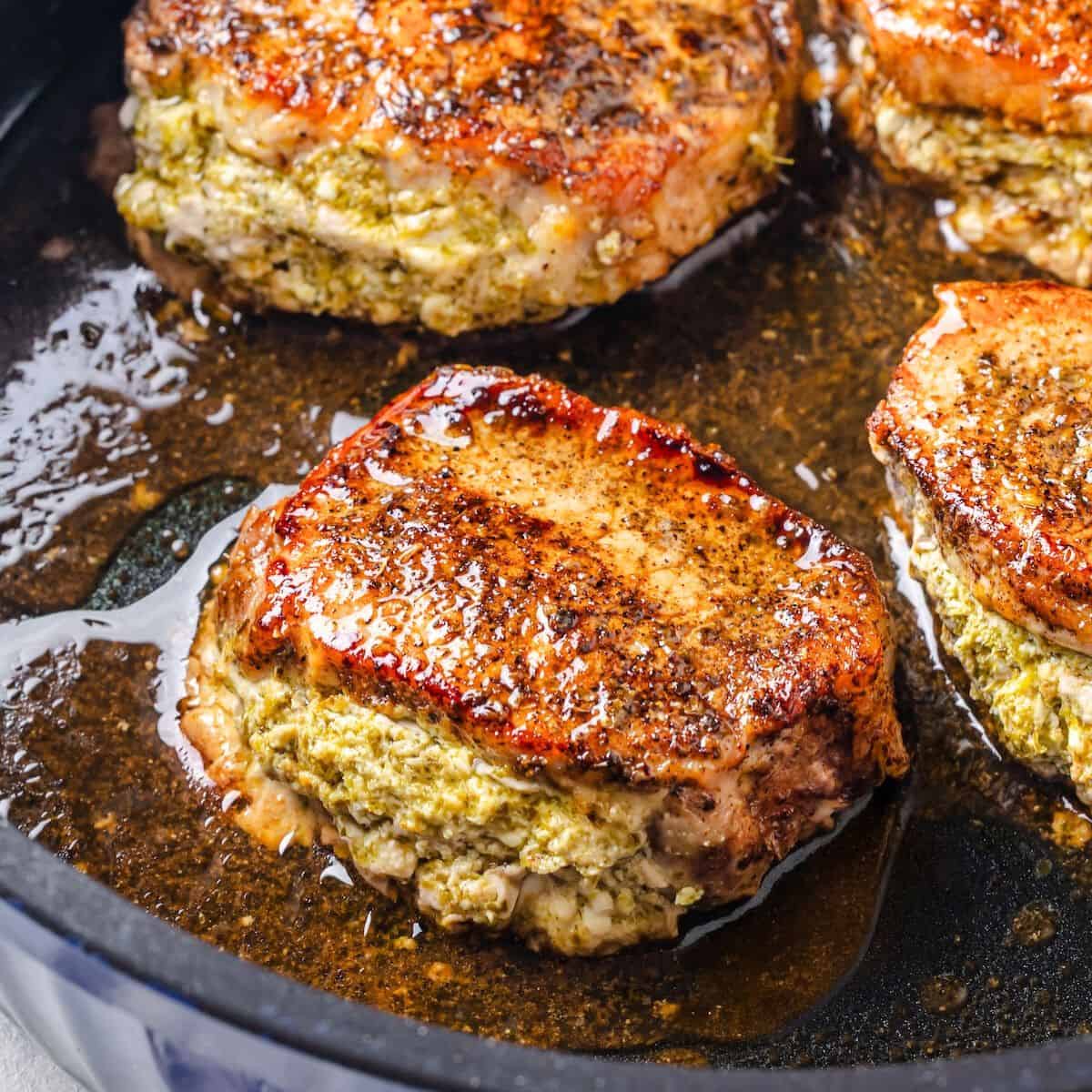 A balsamic vinegar brushed pork chop stuffed with pesto and feta cheese in a blue skillet.