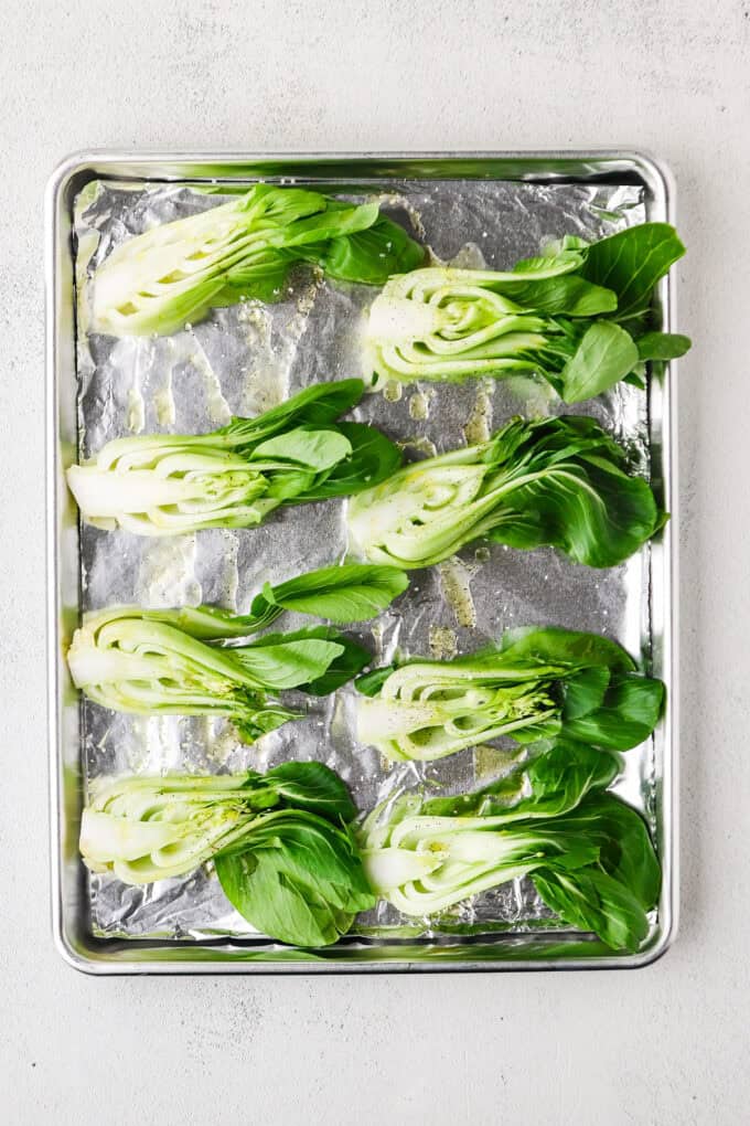 Baby bok choy halved and laid out on a foil lined baking sheet before being cooked.